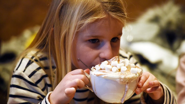 Young girl drinking a large mug of hot chocolate.